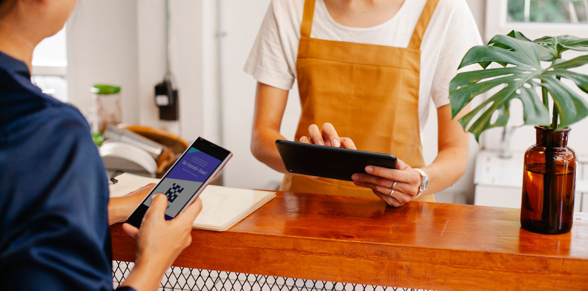 employée d'un café tenant une tablette au comptoir pendant qu'un client règle avec son téléphone