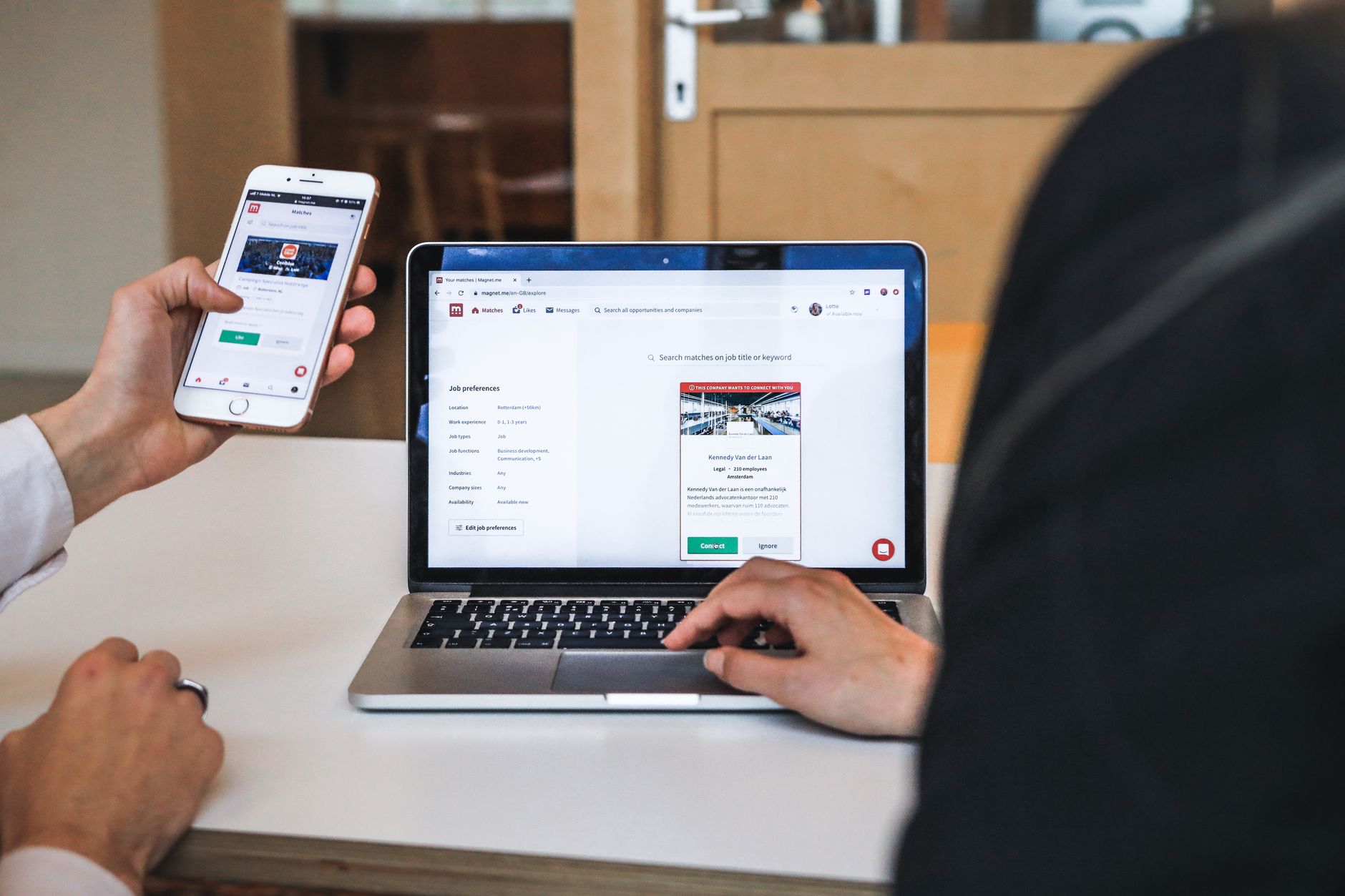 deux personnes consultent un site, l'une sur smartphone, l'autre sur un ordinateur portable posé sur une table blanche