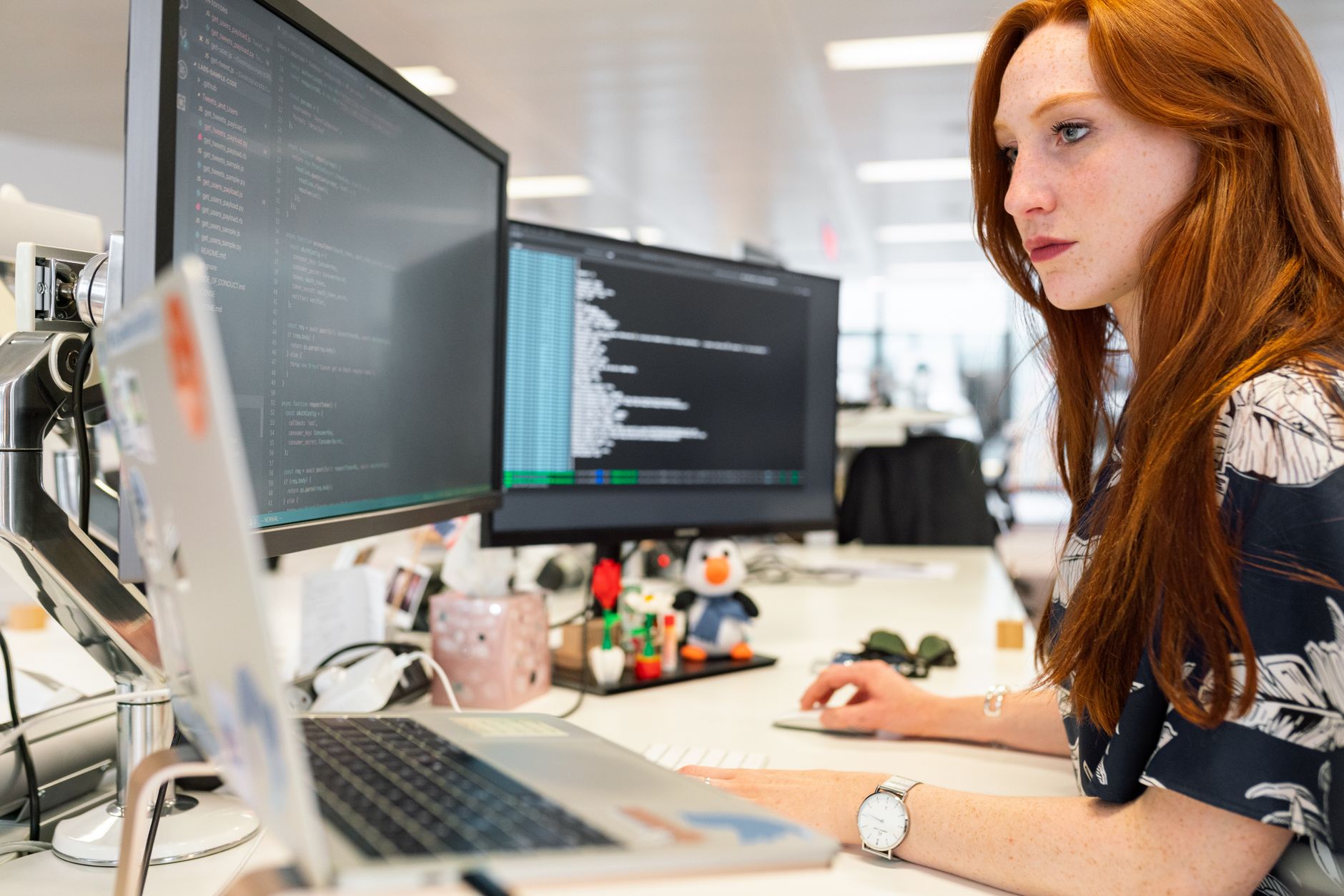 développeuse concentrée devant deux écrans affichant du code, ordinateur portable au premier plan