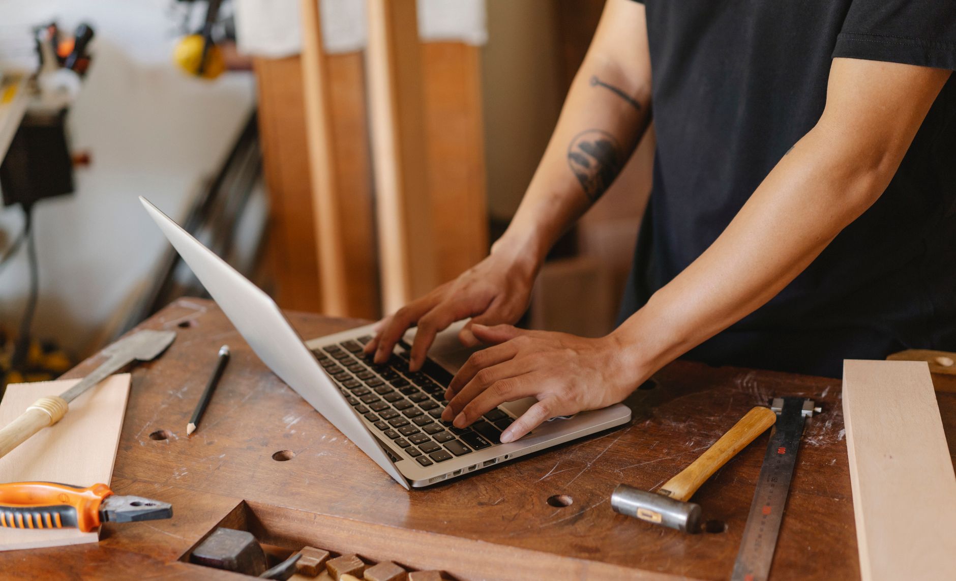 artisan menuisier consultant un ordinateur portable posé sur son établi, entouré d'outils de travail du bois