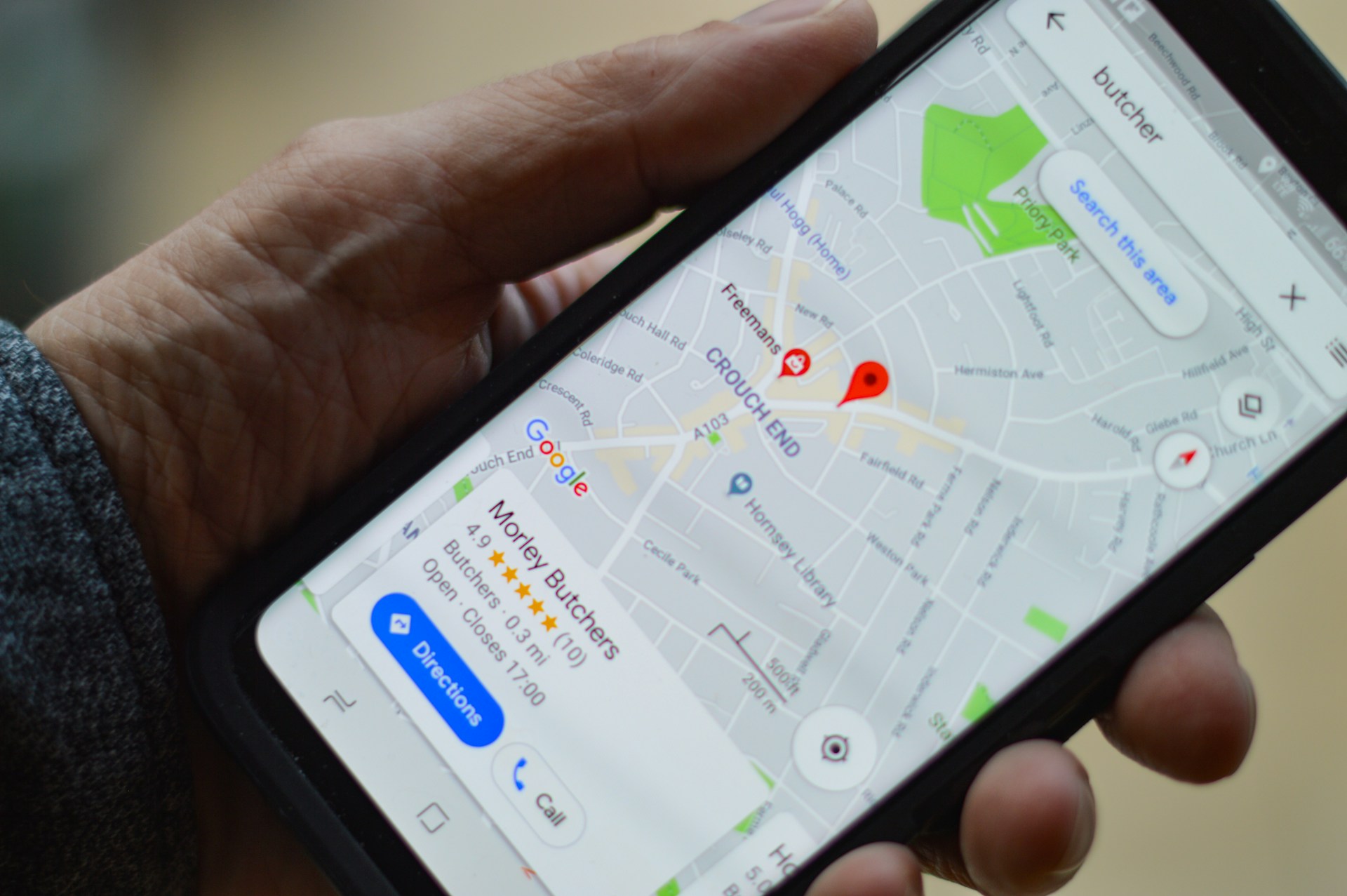 main tenant un smartphone qui affiche Google Maps avec la fiche d'un commerce, sa note en étoiles et ses boutons itinéraire et appel