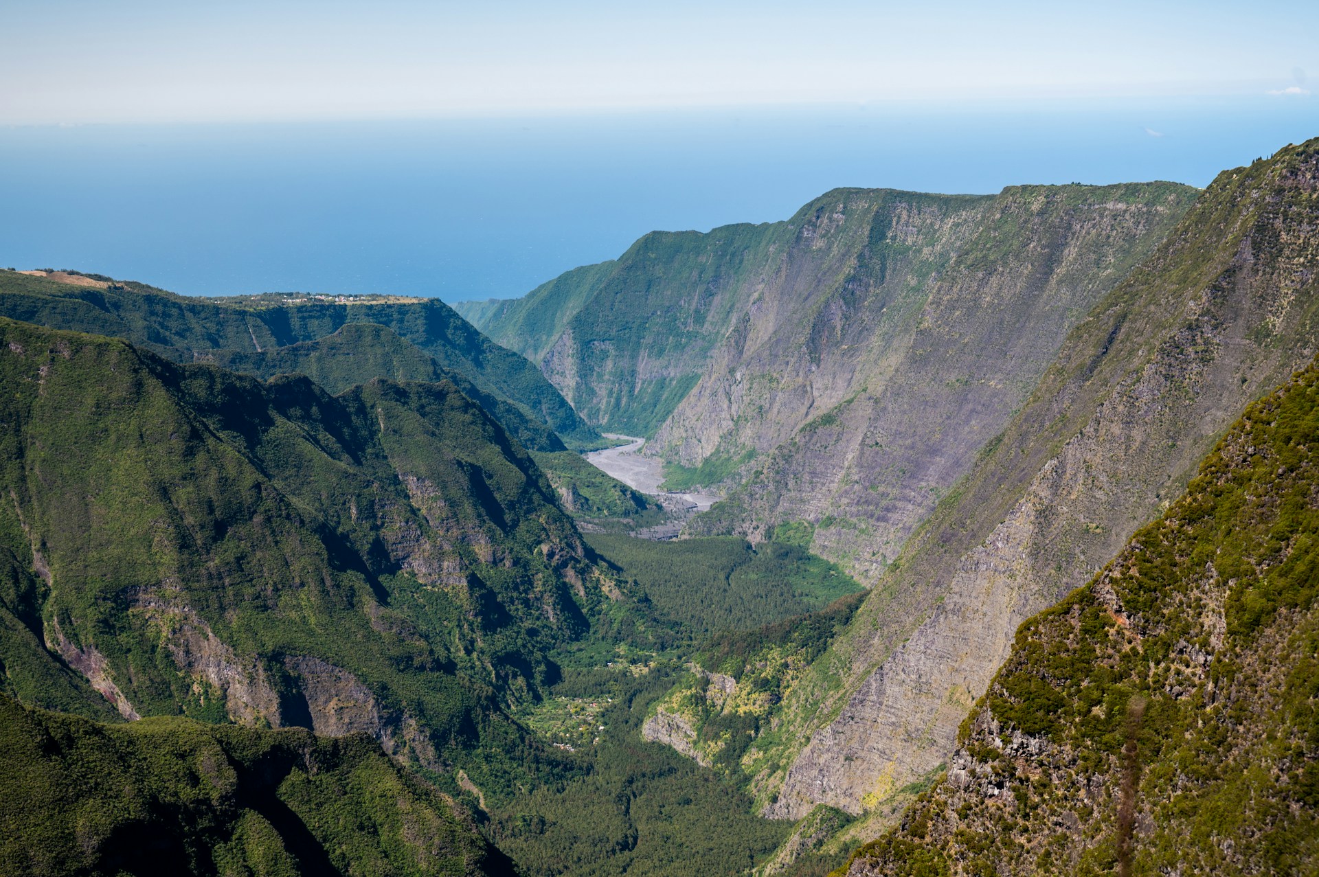 vue plongeante sur une ravine verdoyante de l'île de La Réunion, encadrée de remparts abrupts, avec l'océan à l'horizon